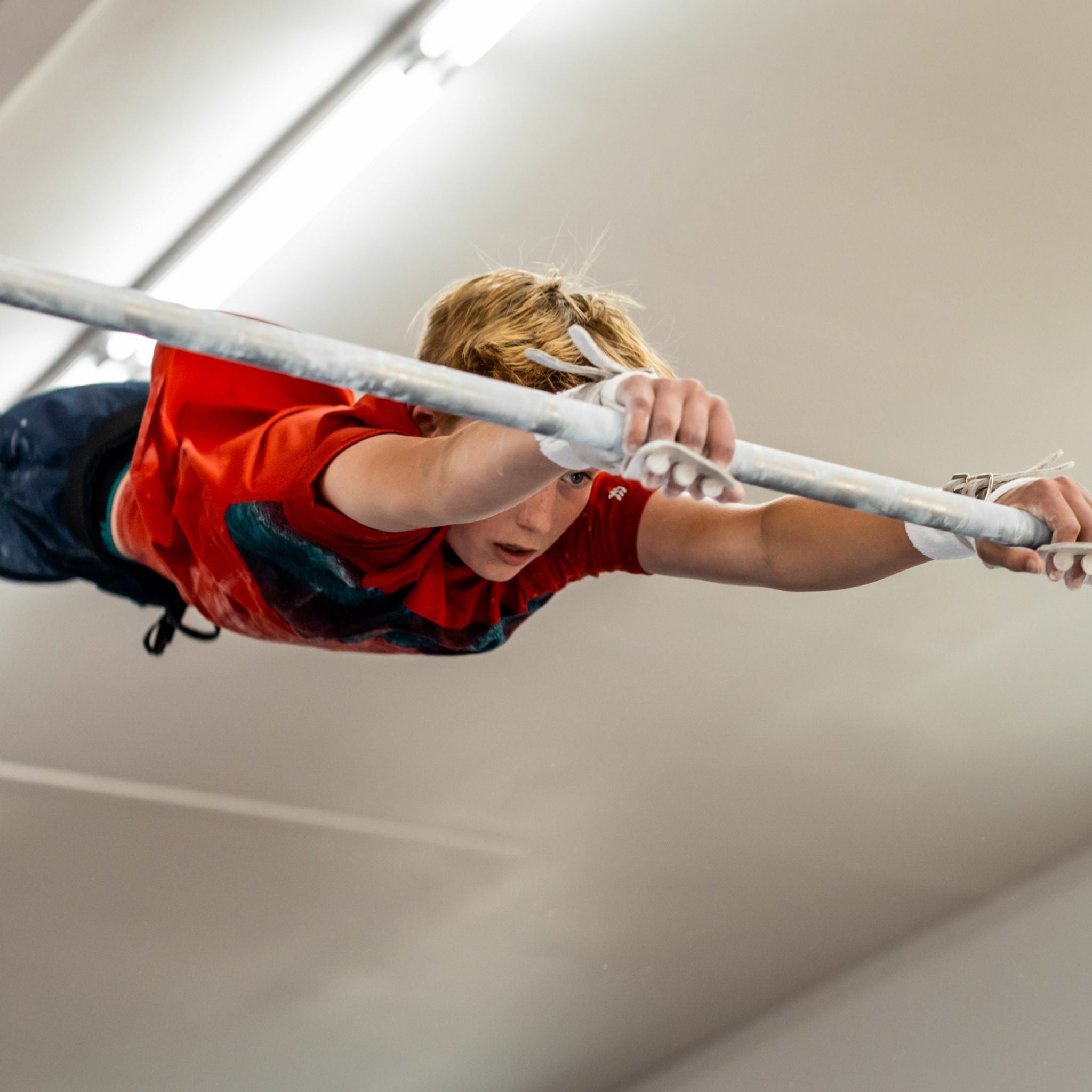 Male gymnast on the high bar wearing Reisport® Men's High Bar Grips - Double Buckle on hands