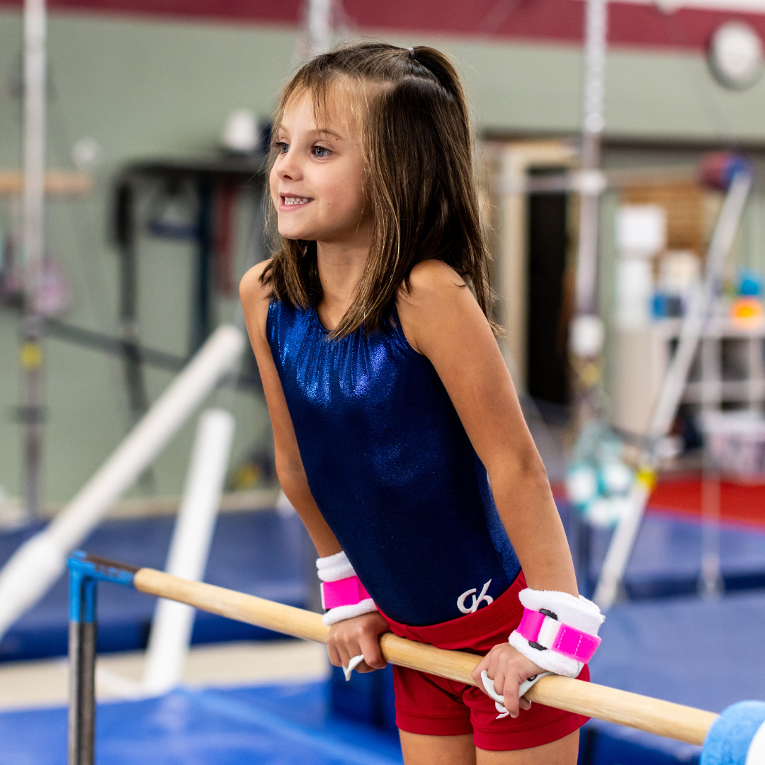 A young girl confidently stands on a balance beam, showcasing her balance and focus during a gymnastics practice.