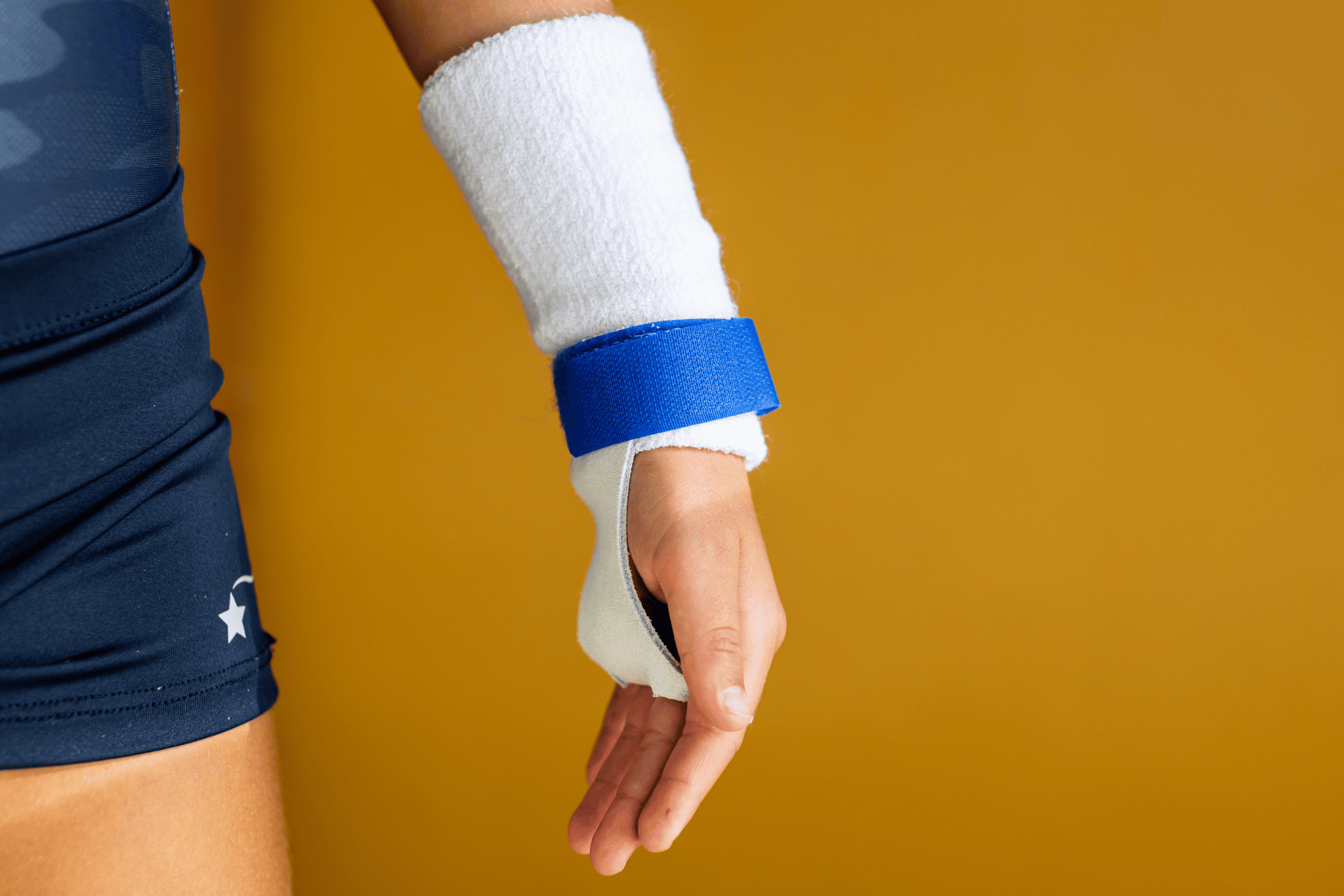 hand wearing blue rainbow grip on yellow background