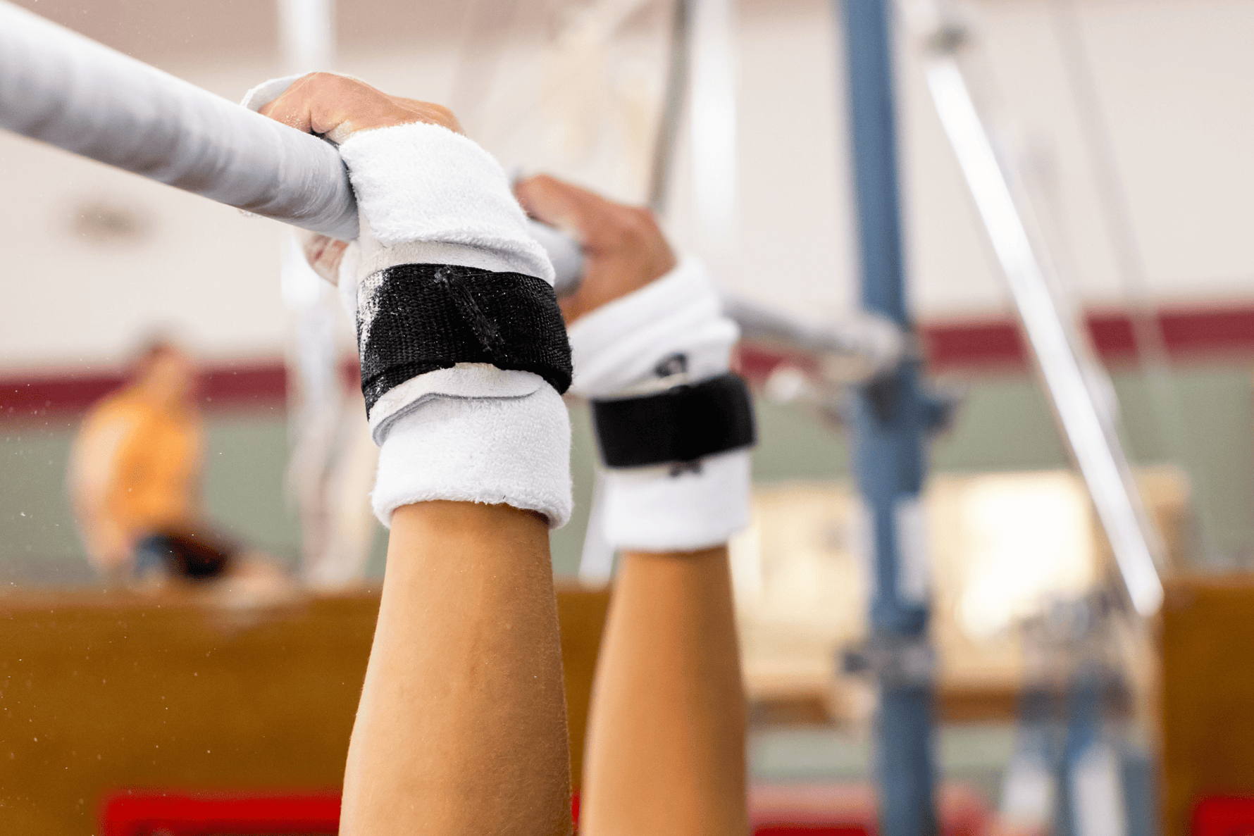 Gibson Summit High Bar hook-and-loop grips on hands hanging from gymnastics bar