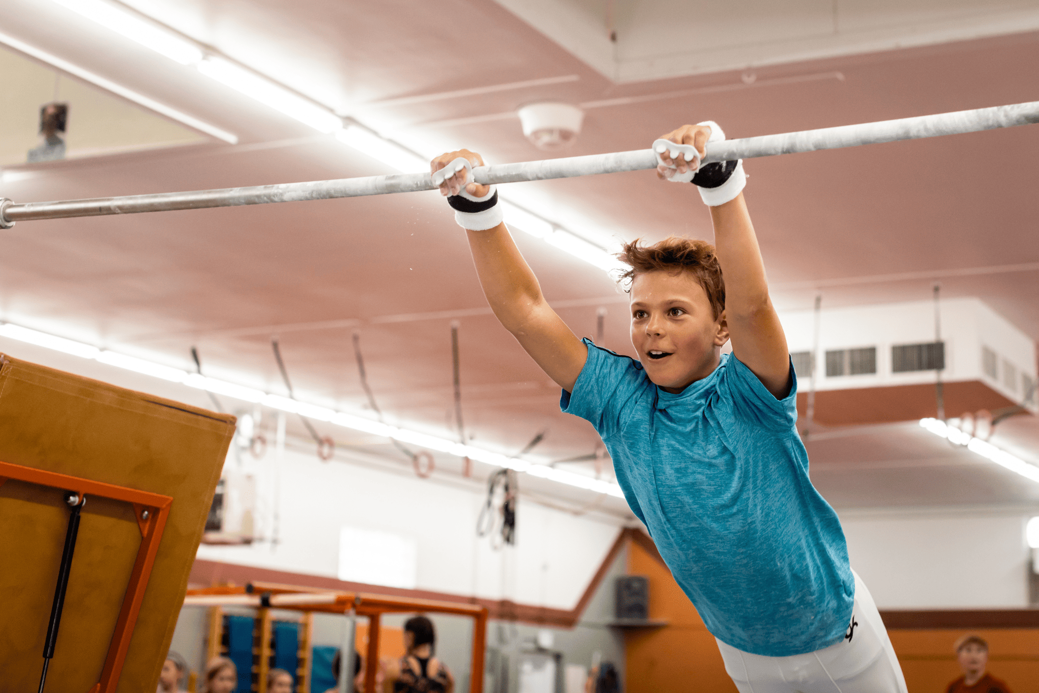 Gibson Summit High Bar hook-and-loop grips on young boy swinging from gymnastics bar